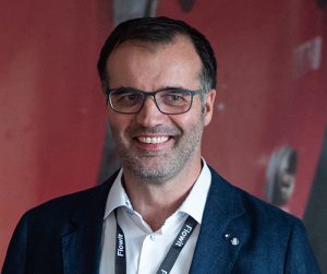 Mann i sort dress og hvit skjorte. Briller og smiler.