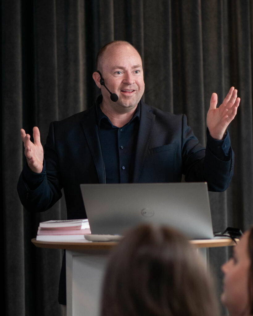 Mann i sort dress på talerstolen og snakker med forsamling