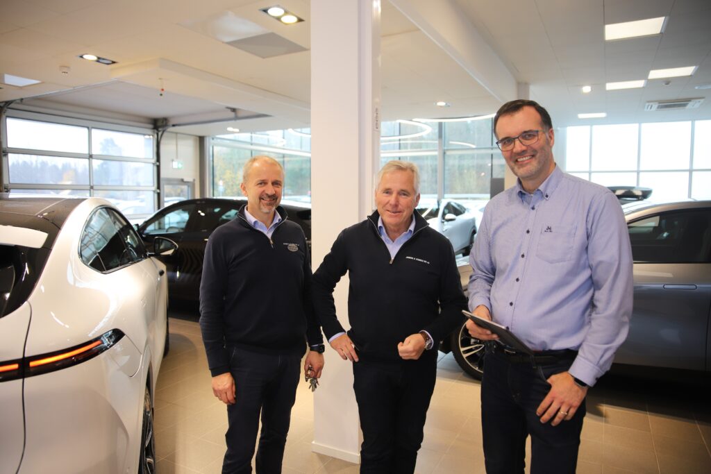 Hos en bilforhandler, 3 personer foran en bil.