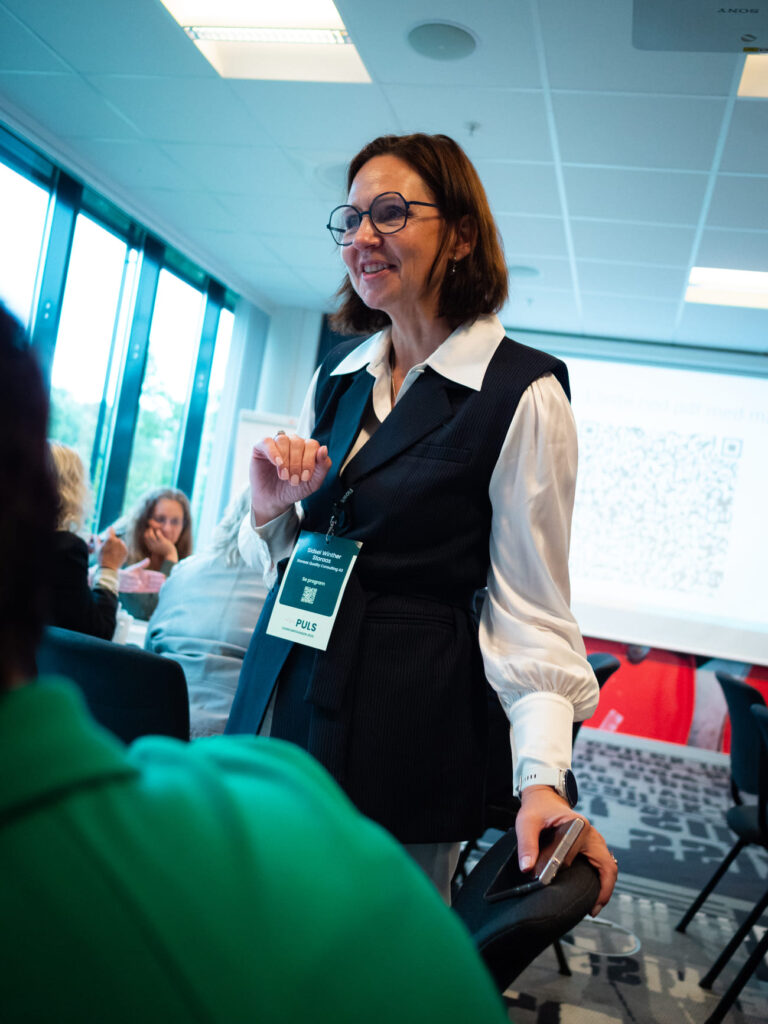 Dame i sort vest og hvit skjorte. Underviser på konferanse.